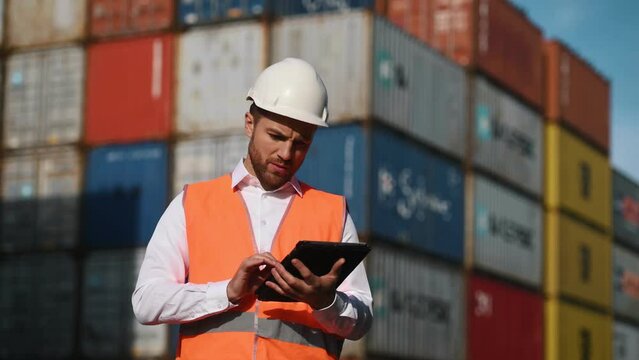 Male worker is on the location with containers, using digital tablet and smiling.
