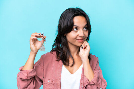 Young hispanic woman holding home keys isolated on blue background thinking an idea while looking up