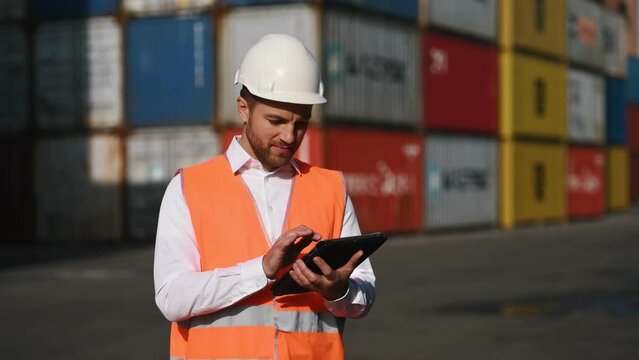 Male worker is on the location with containers, using digital tablet and smiling.