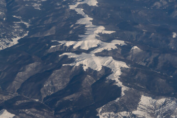 Fototapeta premium Wing of aerial view of an airplane jet flying above clouds from the window in traveling and transportation concept. White snow mountain in winter season. Nature landscape background.