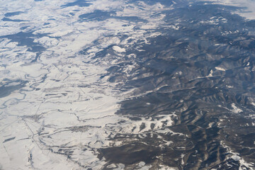 Wing of aerial view of an airplane jet flying above clouds from the window in traveling and transportation concept. White snow mountain in winter season. Nature landscape background.