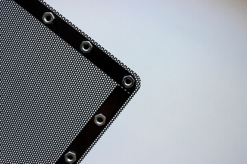 Part of black metal perforated panel with shiny nuts around the edges on white background