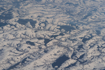 Wing of aerial view of an airplane jet flying above clouds from the window in traveling and transportation concept. White snow mountain in winter season. Nature landscape background.