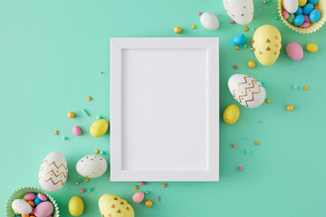 Easter decoration concept. Flat lay photo of white photo frame colorful easter eggs and sprinkles on turquoise background with blank space