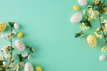 Easter decor concept. Top view photo of white yellow easter eggs cherry blossom branches on turquoise background with copy space in the middle