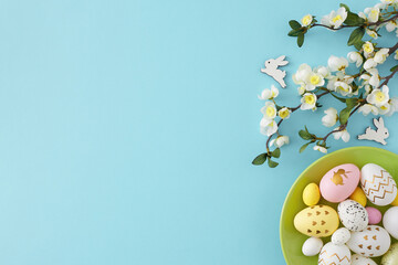 Easter decoration concept. Top view photo of green plate with colorful easter eggs cute rabbit and cherry blossom branch on isolated pastel blue background with empty space