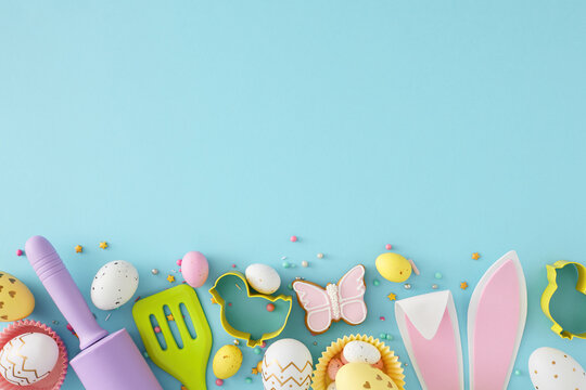 Easter cooking concept. Top view photo of easter bunny ears colorful eggs kitchen utensils baking molds butterfly shaped gingerbread and sprinkles on isolated pastel blue background with empty space