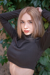 Teenage girl with blonde hair and red lips wears short black turtleneck put her hands behind head...
