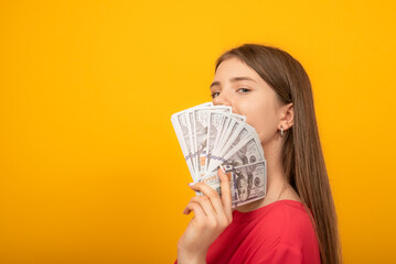 Young woman holds wad of money li fan on a bright yellow orange background. Copy space.