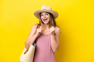 Young caucasian woman holding a beach bag isolated on yellow background celebrating a victory in winner position