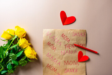 Gelbe Rosen und ein Packpapier mit Mom, Mama und Danke. Muttertag.