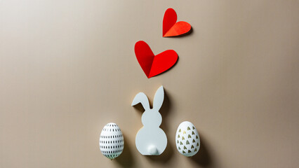 Ein weißer Holz Osterhase, zwei Eier und zwei rote Herzen auf einem beigen Hintergrund. Ostern.