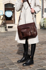 Part photo of a woman with a brown leather briefcase with antique and retro look. Outdoors photo