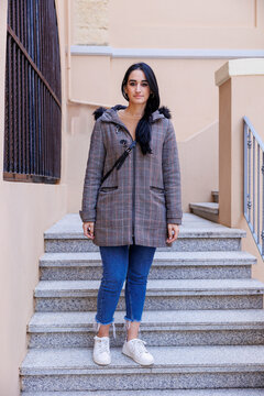 donna mora con i capelli neri  con cappotto e jeans scende le scale in un edificio in esterni