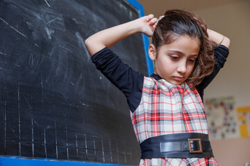 bambina vestita a quadri davanti alla lavagna di una classe si sistema la coda dei capelli 