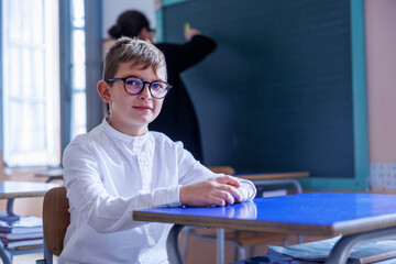 Bambino biondo con gli occhiali  seduto in un aula di una scuola durante alla lezione 