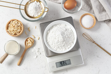 Flour in white bowl measuring on digital scale with cake or bakery ingredients and utensil on marble kitchen table