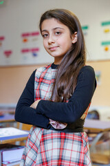 Alunna vestita con un vestito a quadri sta in piedi con le braccia incrociate in un aula di una scuola