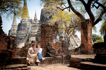 two asian woman holding smart phone in hand sitting in old temple of thailand