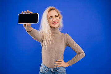 A smiling young woman holds a phone screen to the camera on a blue background. Mockup