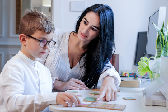 Educatrice con i capelli  scuri applica delle tecniche di apprendimento con un bambino biondo , all'interno di  in uno studio. privato.