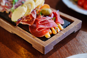a wooden tray with snacks made of dried meat, sausage, cheese and potato chips.
