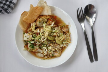 Kupat tahu is a traditional Indonesian food consisting of ketupat and tofu in peanut sauce. Usually include rice cake, tofu, bean sprouts, brown sugar, and prawn crackers. Served in white plate.