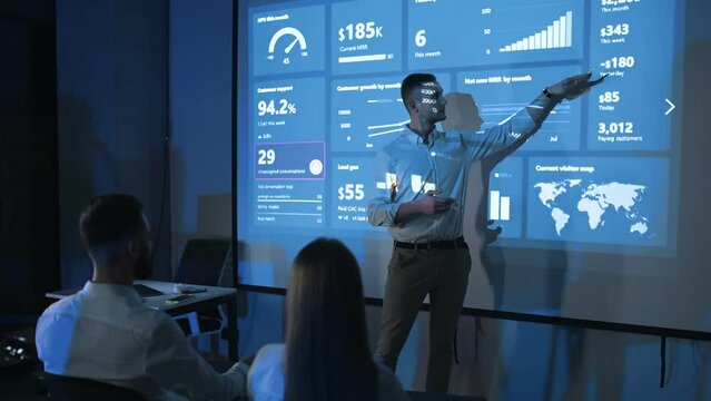 Man in formal clothes is showing business plan on the big projector for the people that sitting and listening.