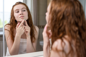 Young teenage girl squeezes out acne looking in the bathroom mirror
