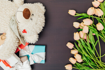 flowers tulips with gifts and toy bear on a dark background