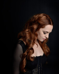 close up portrait of beautiful woman with long red hair wearing sheer corset top. variety of facial expressions,  Isolated on dark studio background with moody silhouette lighting.