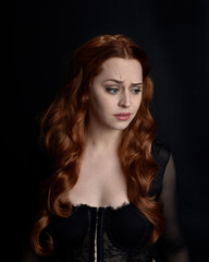 Fototapeta premium close up portrait of beautiful woman with long red hair wearing sheer corset top. variety of facial expressions, Isolated on dark studio background with moody silhouette lighting.