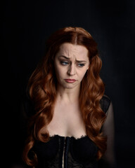 close up portrait of beautiful woman with long red hair wearing sheer corset top. variety of facial expressions,  Isolated on dark studio background with moody silhouette lighting.