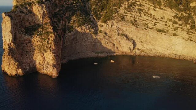 Aerial shot starting big and descending onto a group of people partying in a boat along the Ibiza cliffs.