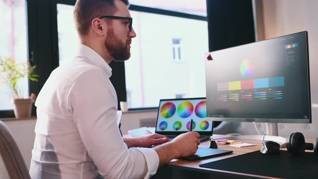 Uses a graphics tablet with a stylus. Male graphic designer is working by computer in the office.