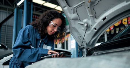 Fototapeta na wymiar Female mechanic uses tablet computer with diagnostics software checking car engine. Specialist inspecting the car in order to find broken components inside the engine bay. Car Service