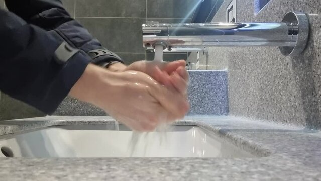 a man washes his hands in the bathroom with modern sink and faucet with motion sensor. plumbing in public places.