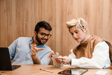 Two coworkers using smartphone while working together in conference room
