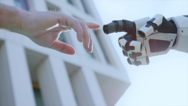 Footage of man's hand and robot hand pointing fingertips on blurred background of white building outdoors. Sunlight, sunny day. Artificial intelligence concept