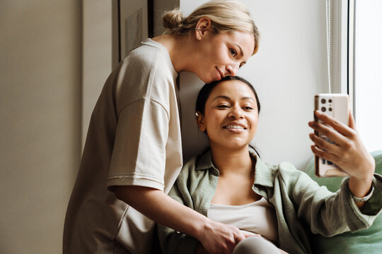 Lesbian couple taking selfie on mobile phone while spending time together at home