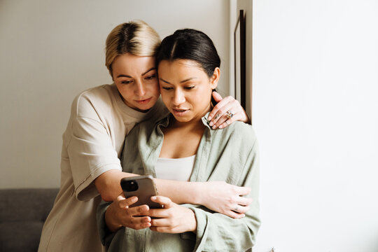 Lesbian couple using mobile phone while spending time together at home