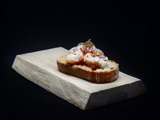 Toast with small shrimps in sauce and herbs, on a wooden board and black background