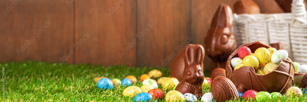 Wall mural Easter egg hunting background. Various candy and chocolate Easter eggs, bunny and rabbits with basket for eggs on green grass park or garden background