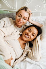 Obraz na płótnie Canvas Joyful pregnant lesbian couple smiling while resting together on bed