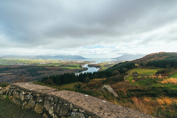Obraz premium Grey cloudy sky, with rolling green hills and vegetation, Slieve Gullion, Co. Armagh, Ring of Gullion, Northern Ireland, showing wall, river and ocean