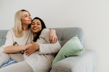 Pregnant lesbian couple embracing while sitting on couch at home
