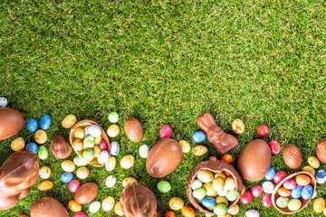 Easter egg hunting background. Various candy and chocolate Easter eggs, bunny and rabbits with basket for eggs on green grass park or garden background