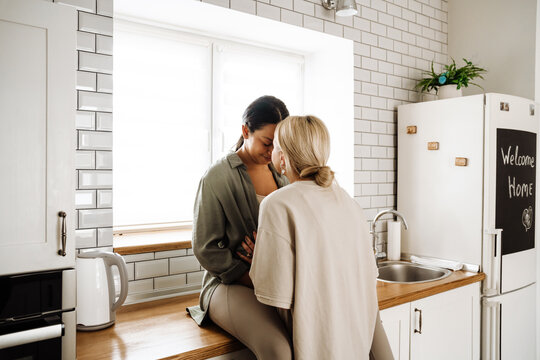 Smiling lesbian couple kissing while spending time together in kitchen