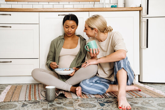 Pregnant lesbian couple having breakfast together while sitting in the kitchen