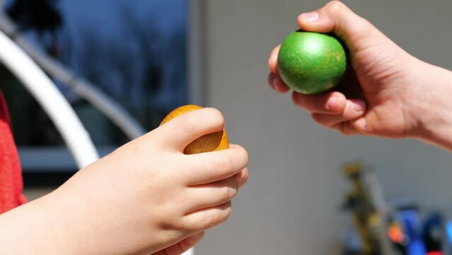 Two kind beat colorful green and orange Easter eggs outdoor. Seasonal tradition games in happy Easter holiday. Close up. Knocking eggs figh game.